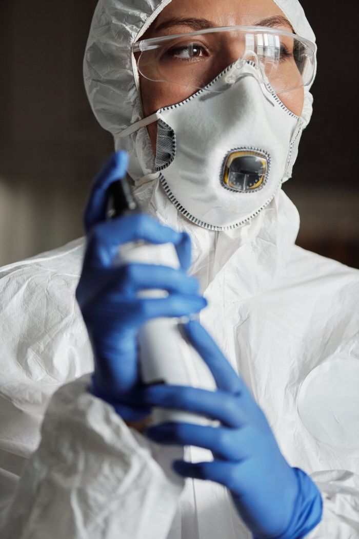 Close-up of a woman in full protective gear holding a disinfectant spray.